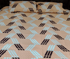 Beige bedspread with black and blue geometric pattern on a bed.