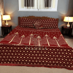 Red and gold patterned bedspread with 'PILORIA' branding on a bed in a bedroom setting.