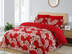 Red floral quilt set on a bed in a bedroom with a window and lamp.