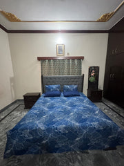 Bedroom with a bed featuring a blue floral patterned comforter, nightstands, and a dresser.