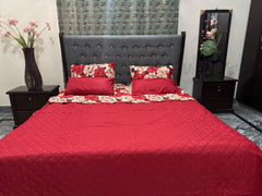 Red quilted bedspread on a bed with matching pillows in a bedroom setting.