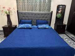 Bedroom with a bed covered in blue bedding and pillows, flanked by nightstands with decorative items.