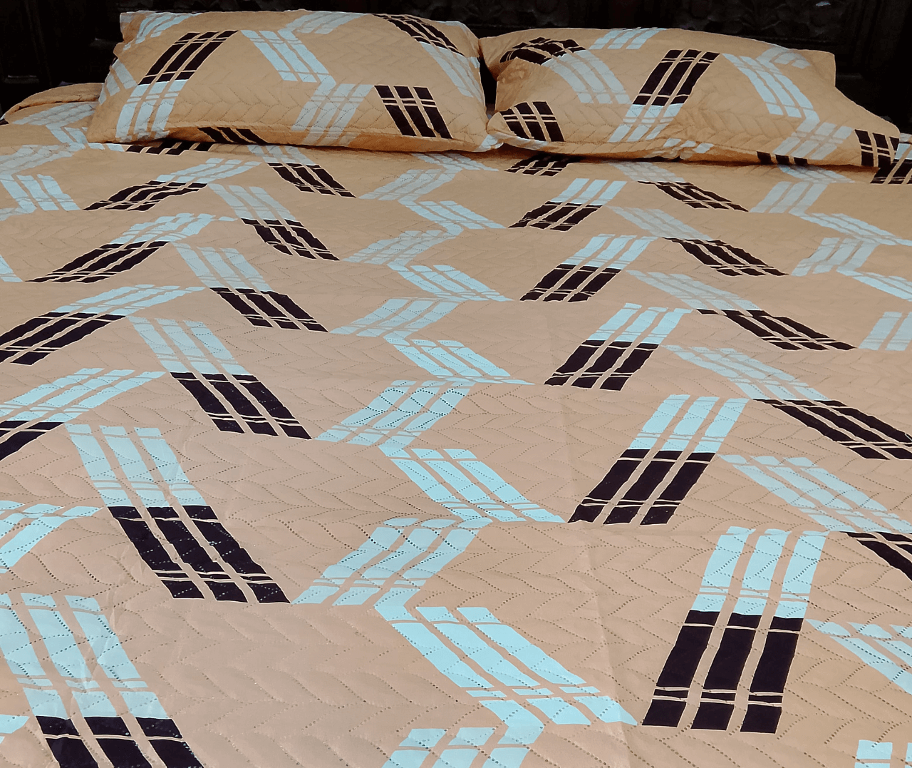 Beige bedspread with black and blue geometric pattern on a bed