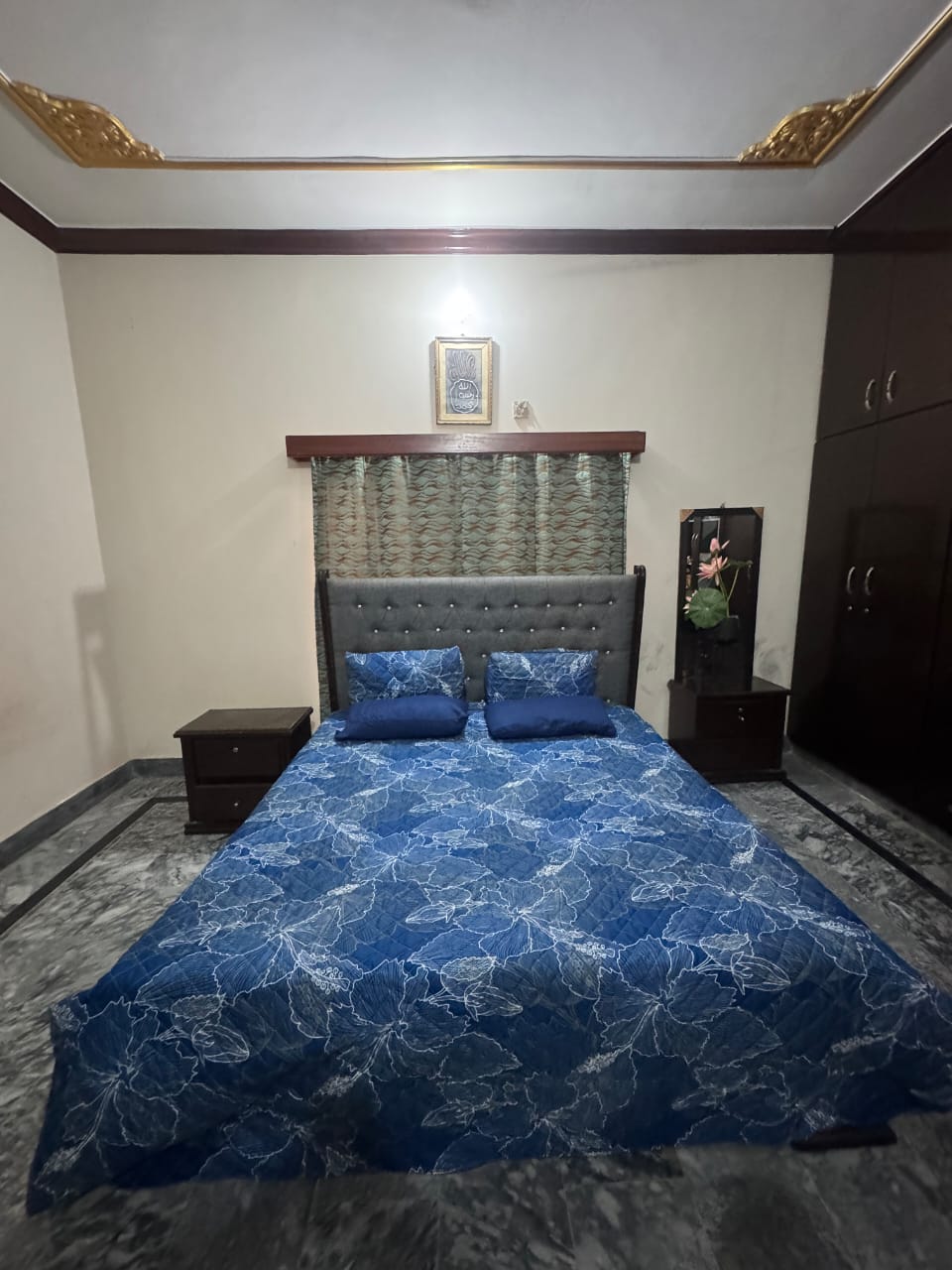Bedroom with a bed featuring a blue floral patterned comforter, nightstands, and a dresser.