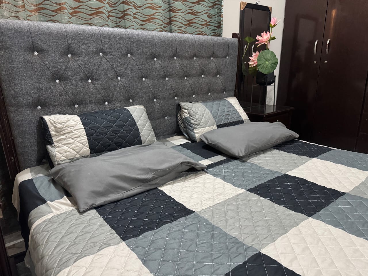 Bed with gray and blue checkered bedding and tufted headboard in a bedroom setting.