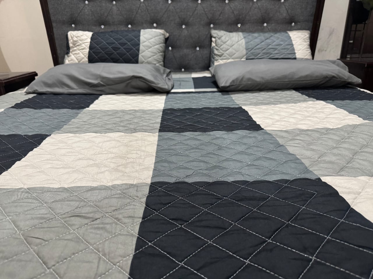 Bed with a checkered quilt in gray, blue, and white patterns.