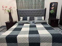 Bedroom with a bed featuring a gray checkered comforter, two nightstands with vases, and a patterned rug.