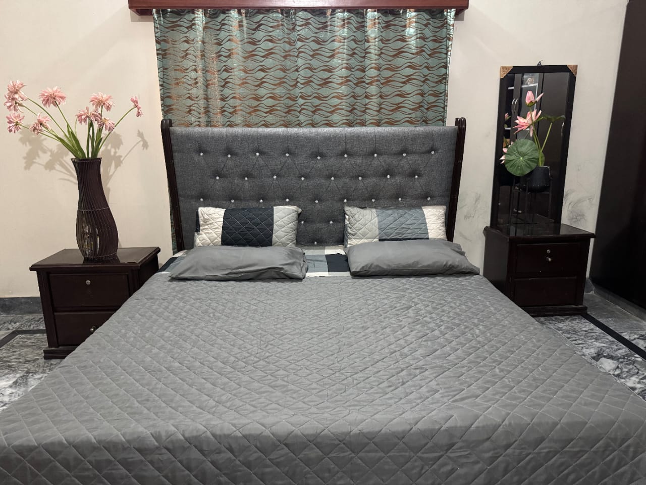 Bedroom with a gray bedspread, pillows, and nightstands with decorative items.