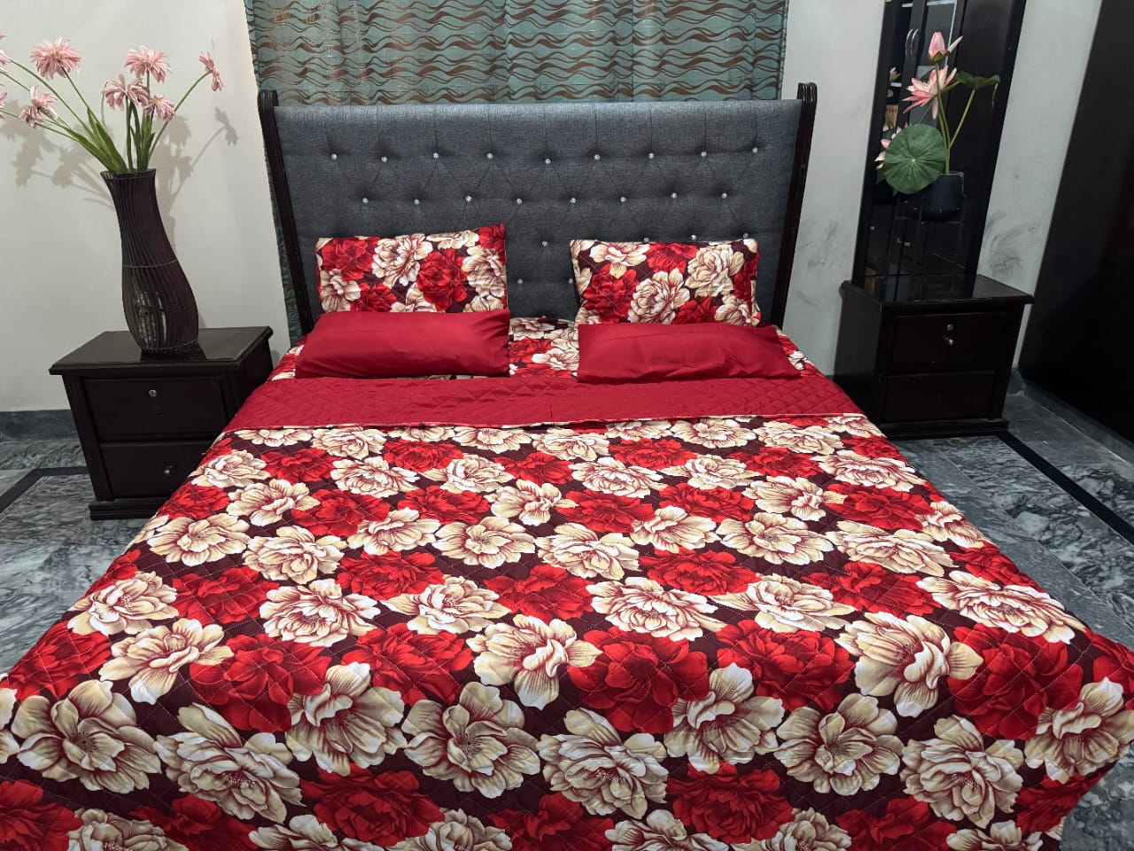 Red and beige floral bedspread on a bed with matching pillows, set against a gray upholstered headboard.