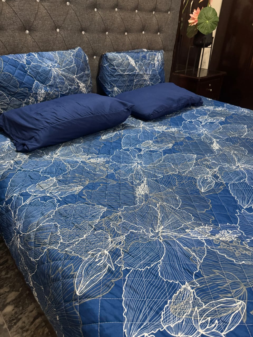 Blue floral patterned bedspread on a bed with matching pillows.